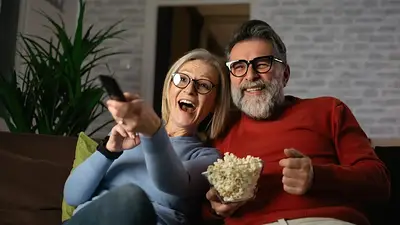 Dos personas ven televisión en su sofá y comen pochoclos Dos personas ven televisión en su sofá y comen pochoclos