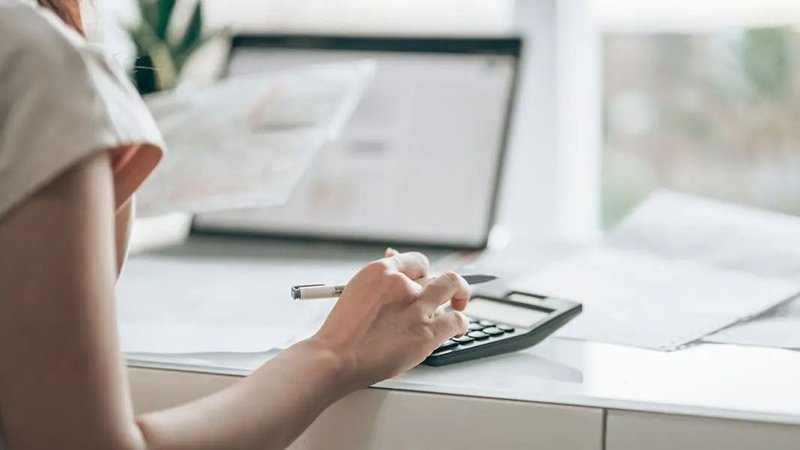 Persona con calculadora, papeles y una notebook