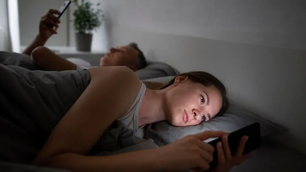 Un hombre y una mujer usando el celular en la cama