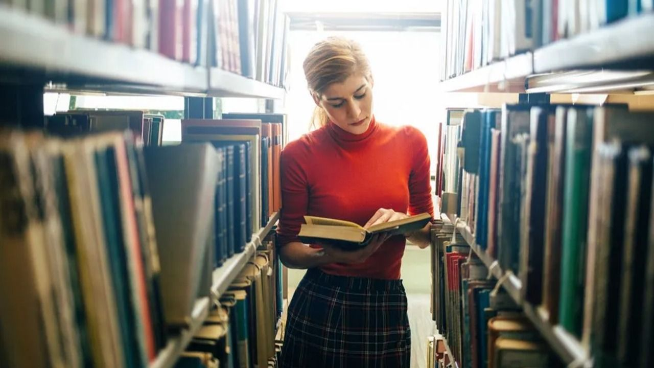 Una chica leyendo un libro en el pasillo de una biblioteca