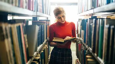 Una chica leyendo un libro en el pasillo de una biblioteca Una chica leyendo un libro en el pasillo de una biblioteca