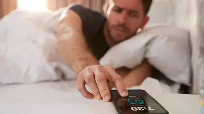 Un hombre apagando la alarma del celular desde la cama Un hombre apagando la alarma del celular desde la cama
