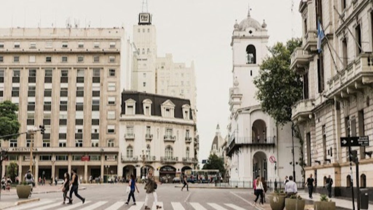 Vista de la Plaza de Mayo, Buenos Aires, con peatones cruzando y edificios históricos al fondo