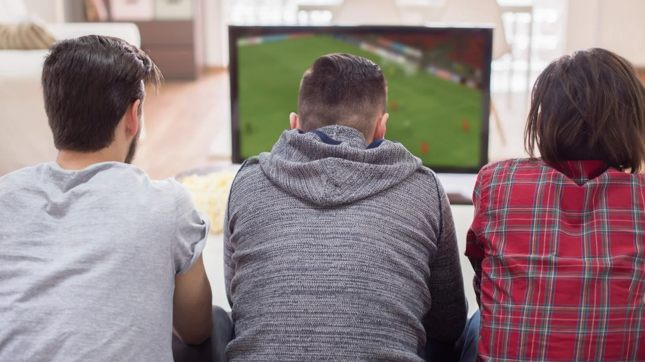 Tres personas mirando un partido de fútbol por televisión en una sala de estar
