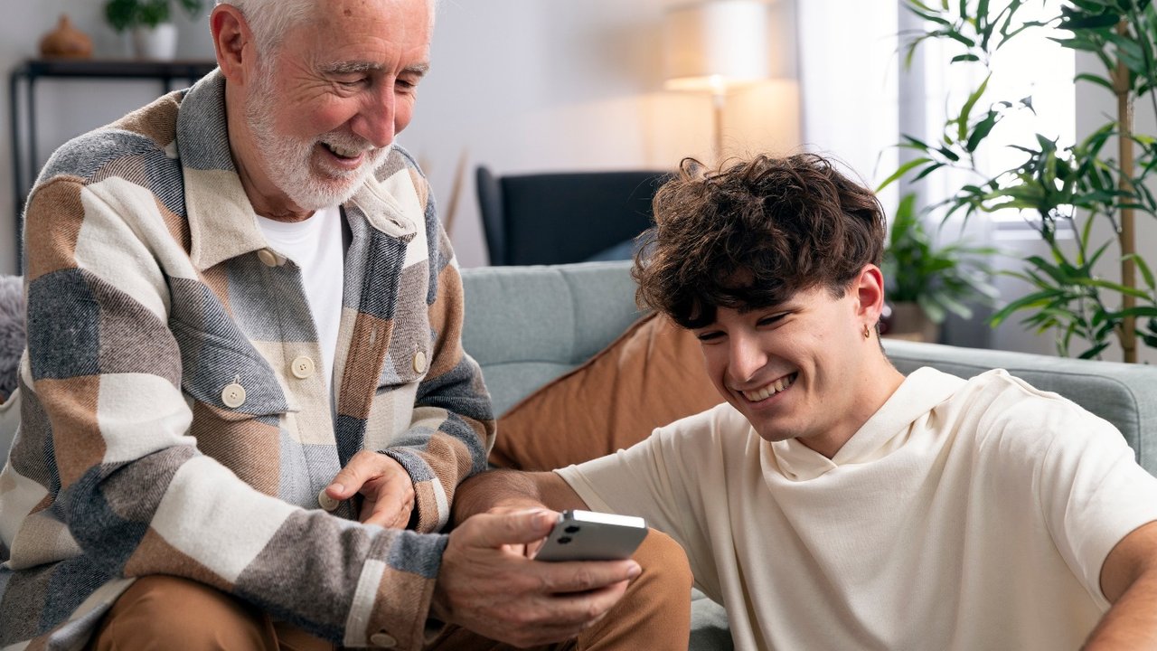 Un hombre mayor y un joven viendo un celular