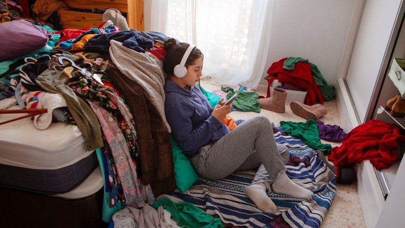 Una chica escuchando música en una habitación desordenada