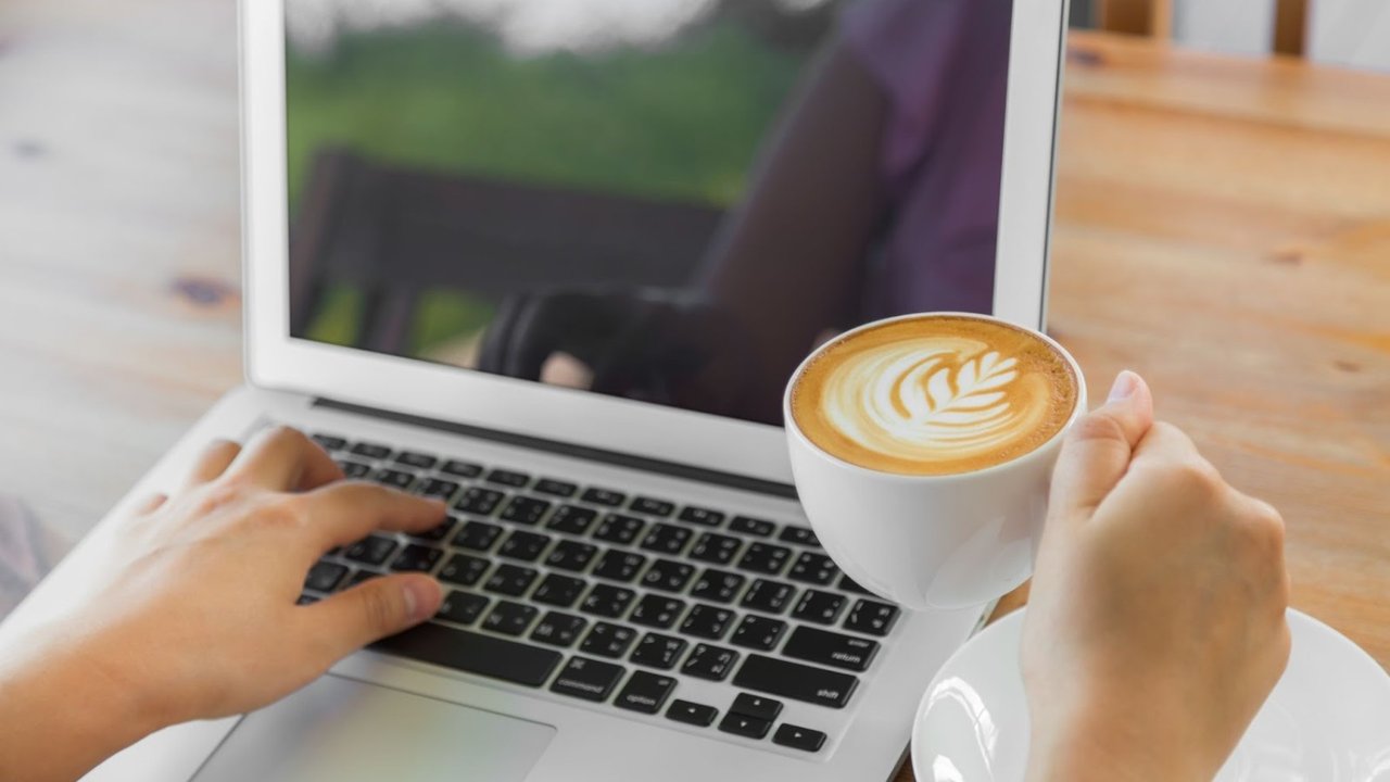 Persona usando una notebook mientras sostiene una taza de café, trabajo freelance en entorno digital