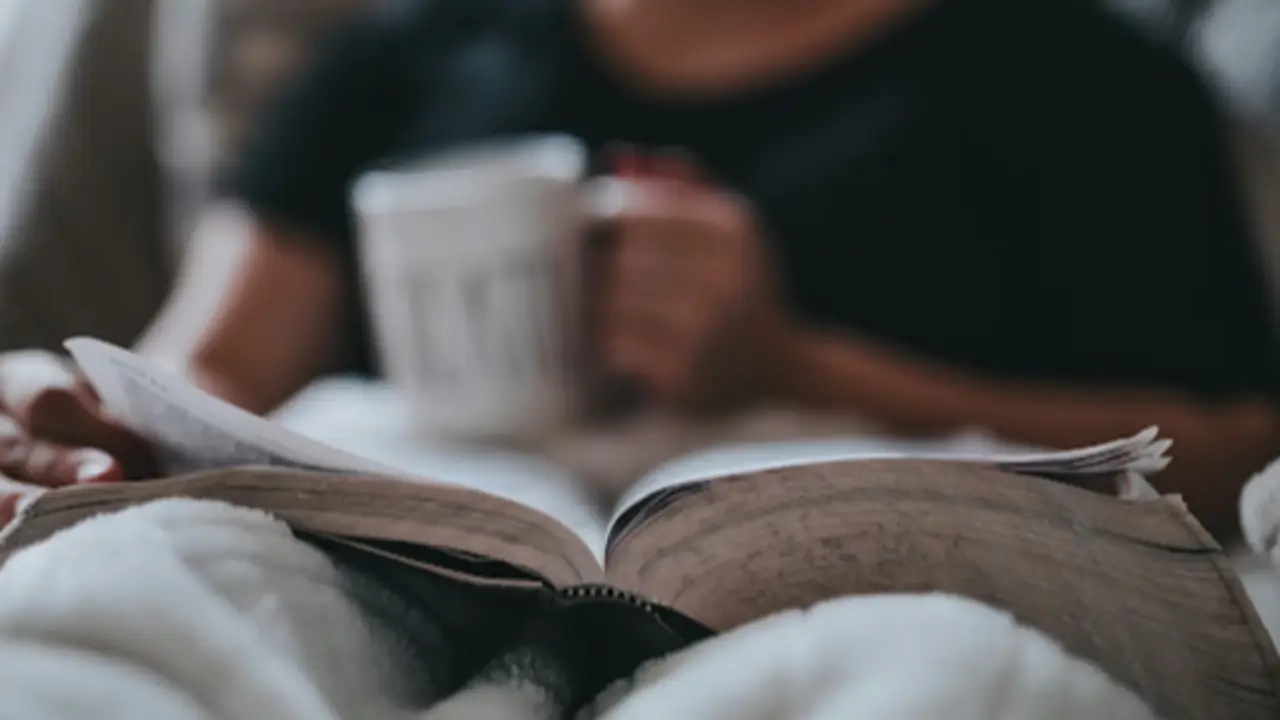 Persona lee un libro en casa mientras descansa con una taza en la mano