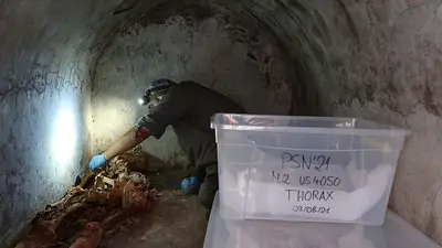 Un arqueólogo trabaja junto a un esqueleto parcialmente momificado en un lugar de sepultura Un arqueólogo trabaja junto a un esqueleto parcialmente momificado en un lugar de sepultura