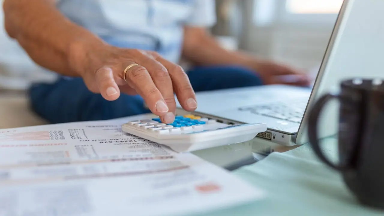 Persona calcula impuestos con una calculadora, papeles y una notebook