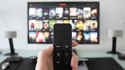 mano sostiene control remoto y un televisor al fondo en un living mano sostiene control remoto y un televisor al fondo en un living